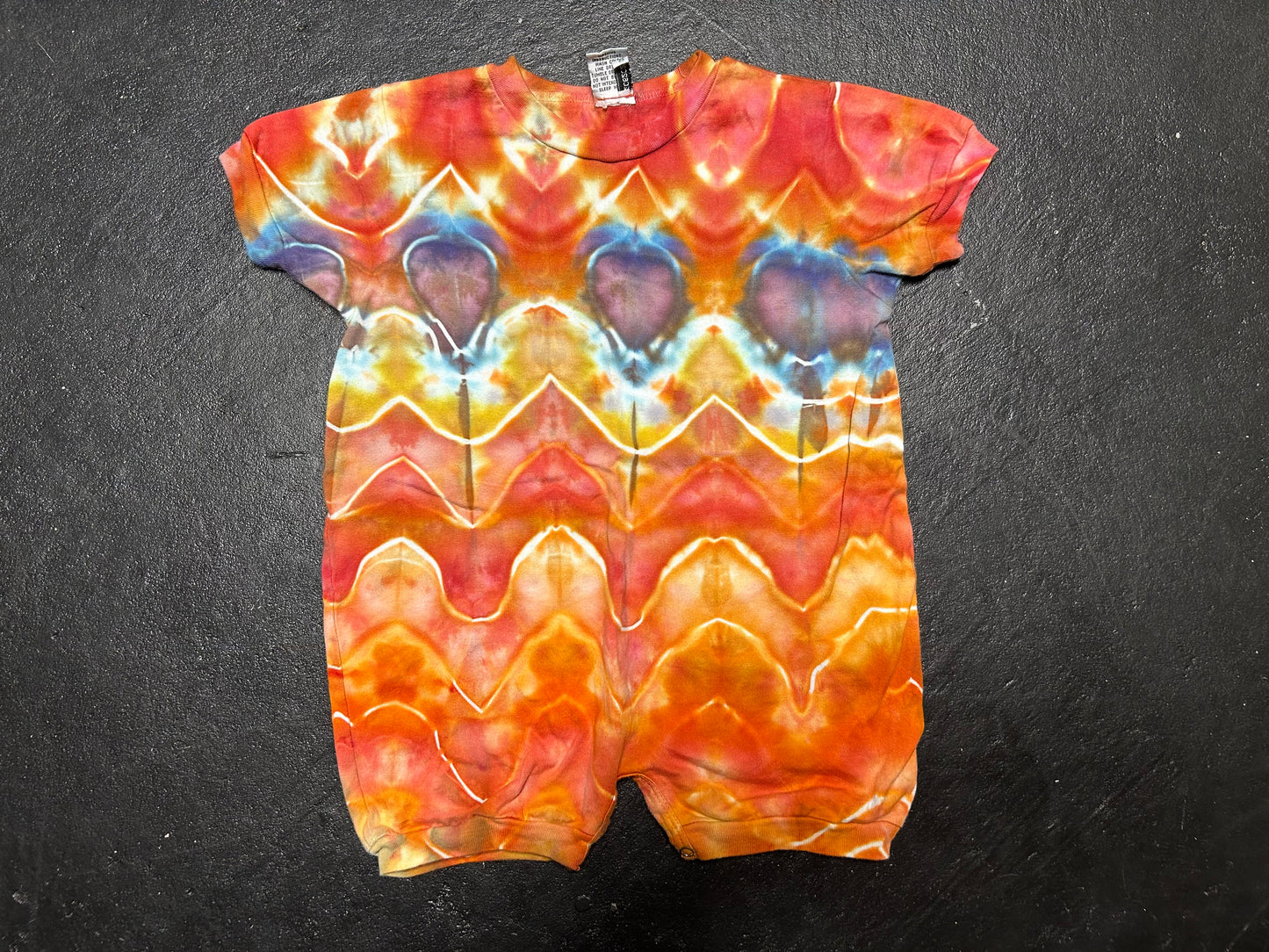 Tie-dye baby romper with wavy pattern on a dark background