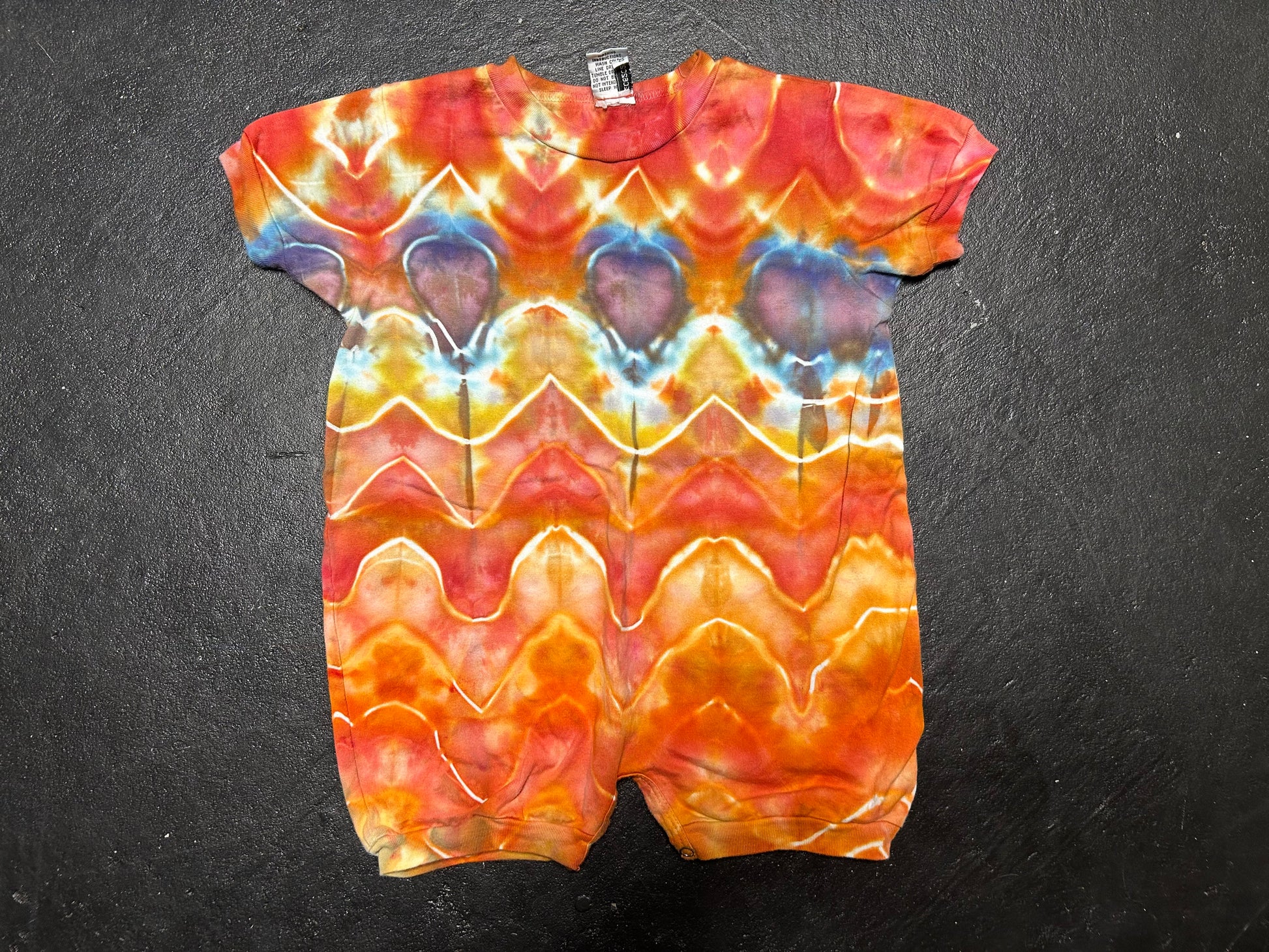 Tie-dye baby romper with wavy pattern on a dark background